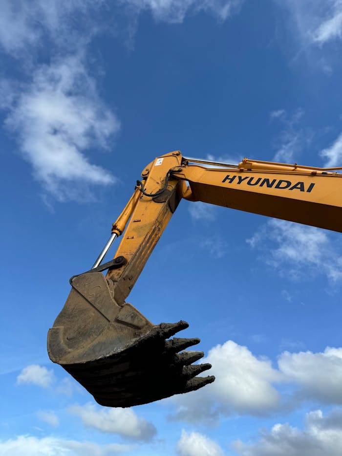 Close-up view of an excavator arm and bucket against a bright blue sky.