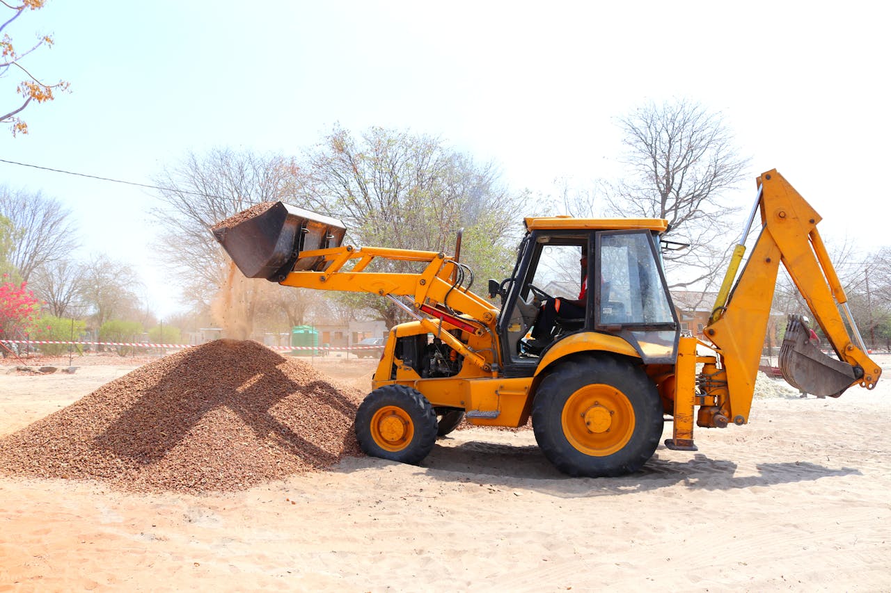 A yellow excavator moving gravel at an outdoor construction site during the day with clear skies.